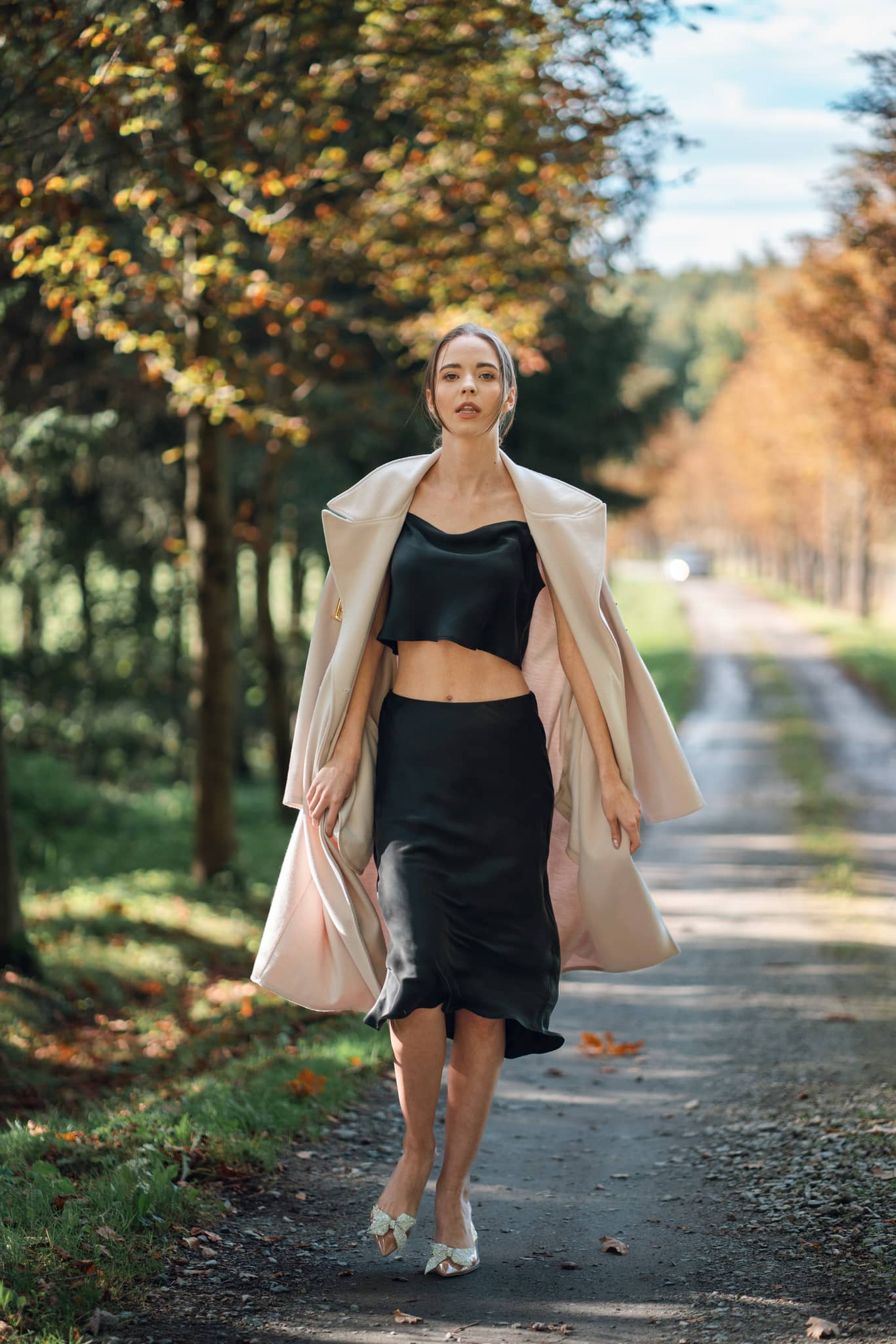 Woman wearing Silk Closet black cropped silk cami and matching silk skirt. Wearing jacket outdoors.